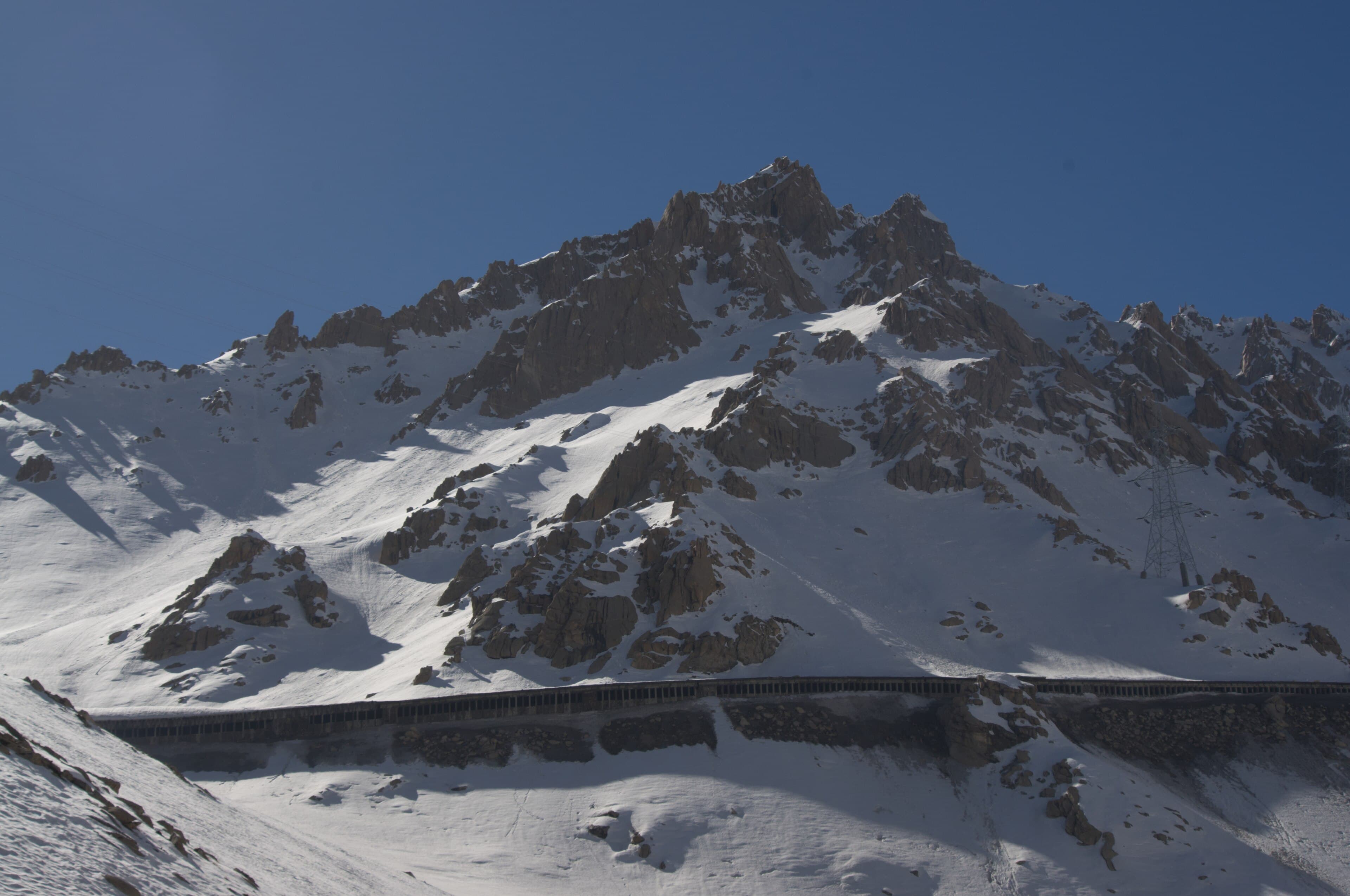 A winding mountain road crossing a snow-covered high pass in the Hindu Kush